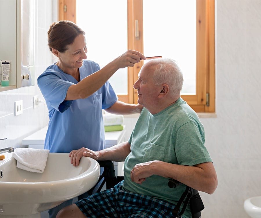 Hospice care volunteer brushes elderly patient's hair in bathroom.