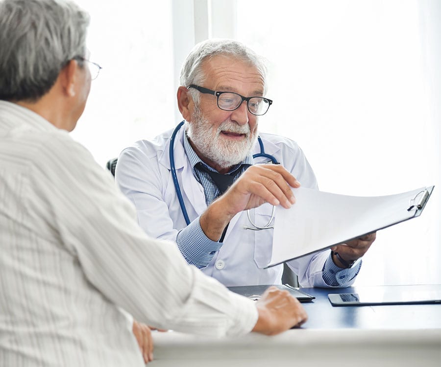 Doctor reviews clipboard chart documents with patient in office.